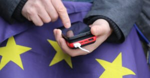 A hand texting on a phone, with the EU flag in the background.